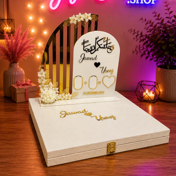 Personalized tombstone wedding decoration set on a cream-colored presentation box with gold accents, placed on a wooden table with warm string lights and decorative plants in the background.