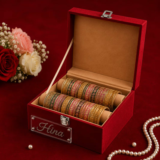 An open red velvet jewelry box with a silver-accented nameplate reading 'Hina' on the front. Inside, two rolls of stacked bangles are neatly arranged.