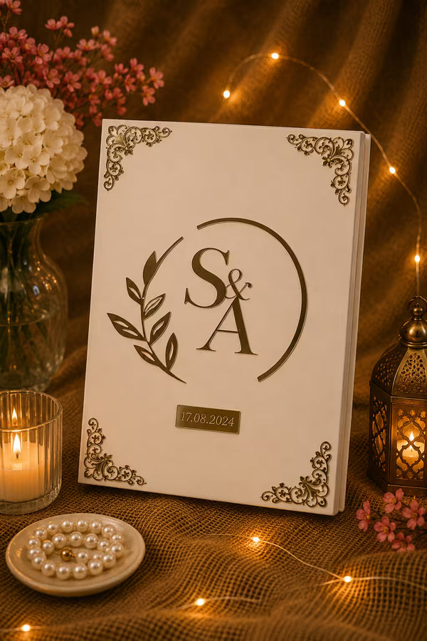 A personalized wedding guest book with a cream cover, featuring a laser-cut monogram 'S&A' with a leaf wreath and the date '17.08.